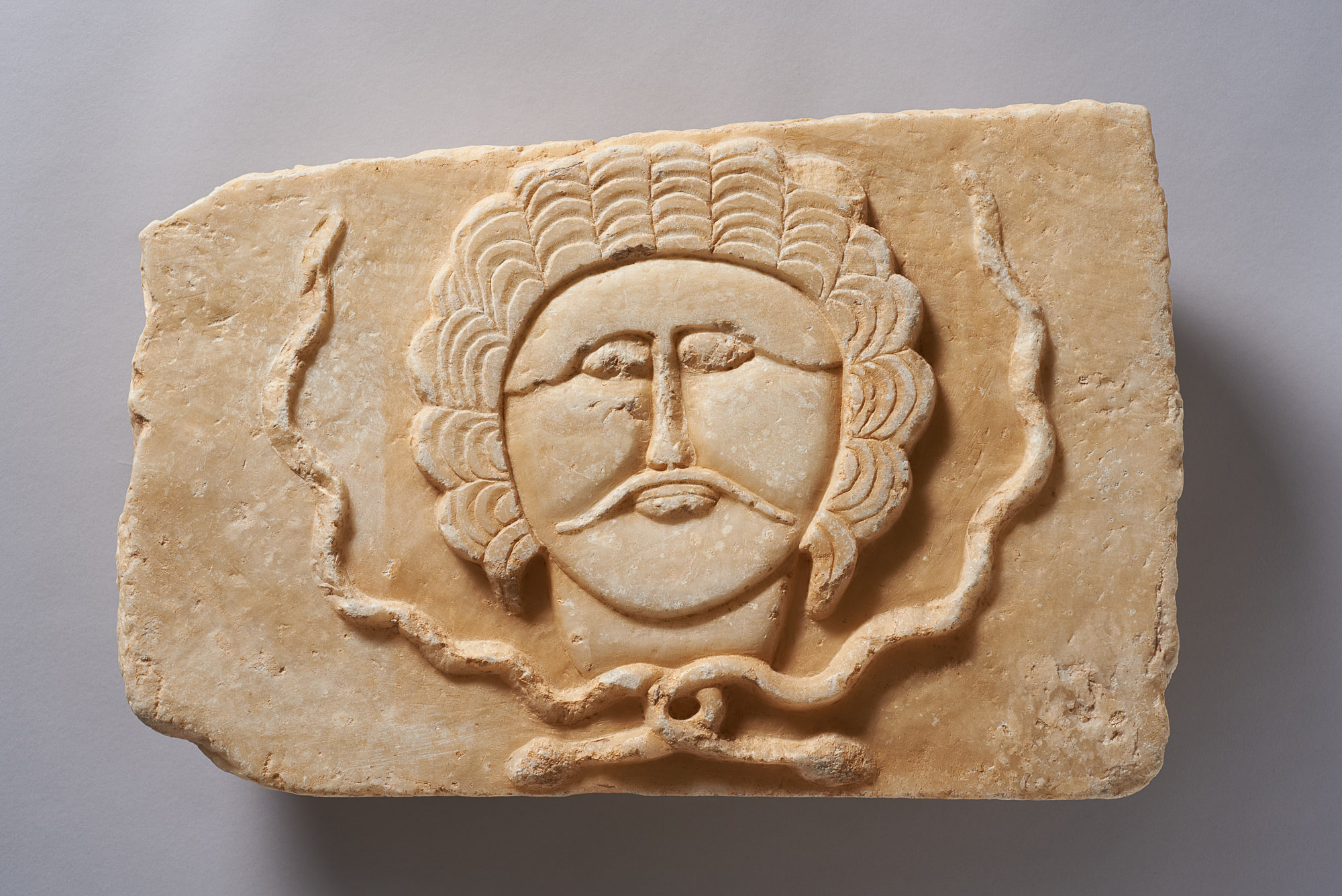 Relief eines Mannes mit Schnurrbart und Haarkranz